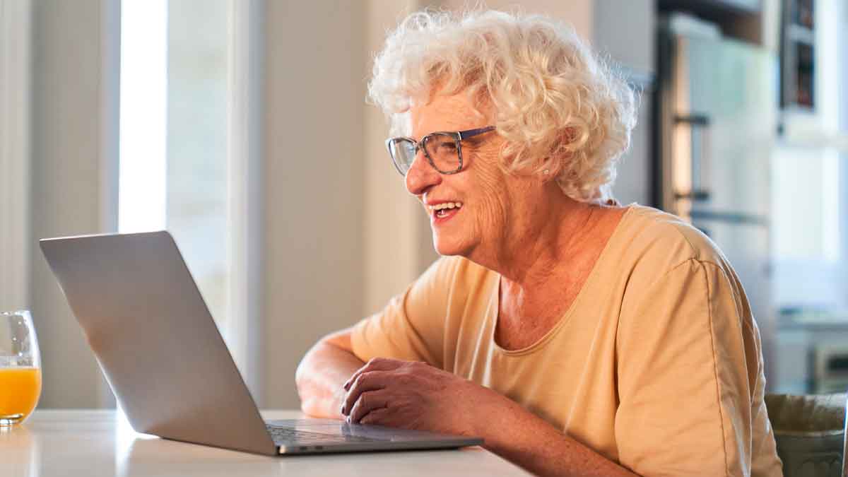 Mujer mayor de 65 años sonríe frente a un portátil mientras realiza online los trámites gratuitos disponibles en 2025