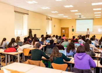 Aula universitaria llena de estudiantes con portátiles escuchando al profesor, frente al debate Universidad vs. FP para lograr empleo rápido