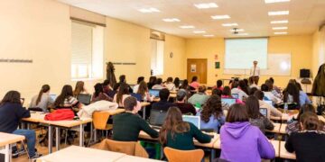 Aula universitaria llena de estudiantes con portátiles escuchando al profesor, frente al debate Universidad vs. FP para lograr empleo rápido