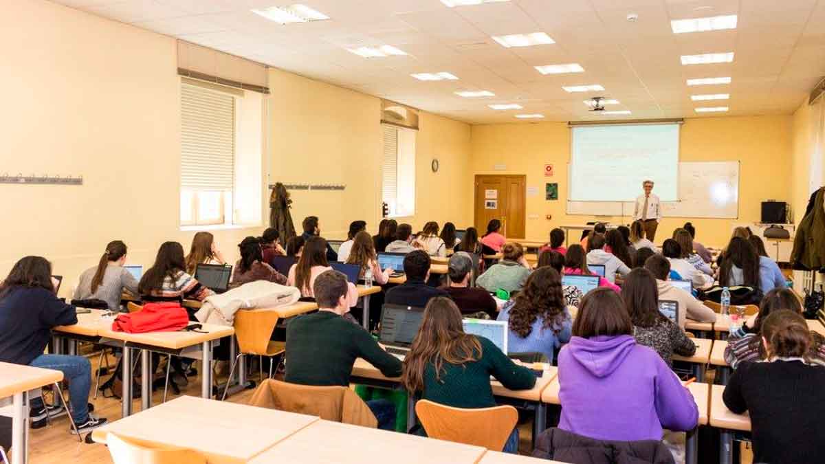 Aula universitaria llena de estudiantes con portátiles escuchando al profesor, frente al debate Universidad vs. FP para lograr empleo rápido
