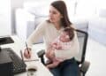 Madre autónoma teletrabajando con su bebé en brazos, ejemplo de las ayudas de maternidad 2025 que ATA reclama reforzar.