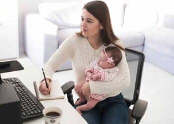Madre autónoma teletrabajando con su bebé en brazos, ejemplo de las ayudas de maternidad 2025 que ATA reclama reforzar.