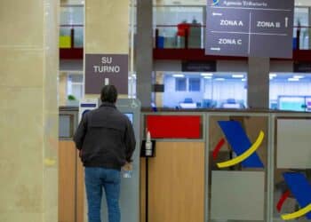 Persona en la Agencia Tributaria gestionando su turno para realizar trámites de tributos municipales.