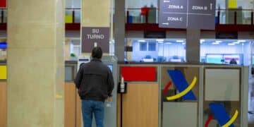 Persona en la Agencia Tributaria gestionando su turno para realizar trámites de tributos municipales.