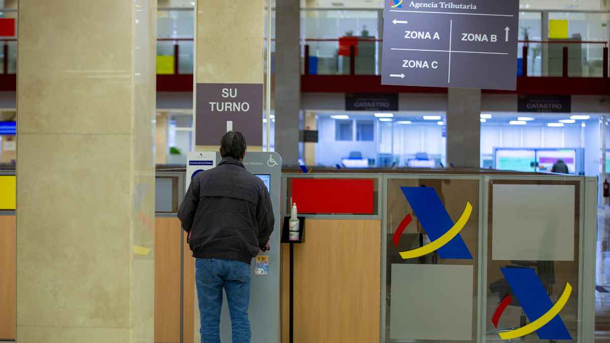 Persona en la Agencia Tributaria gestionando su turno para realizar trámites de tributos municipales.