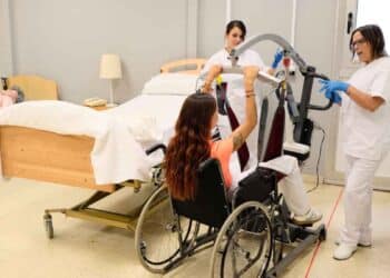 Formación en atención sociosanitaria, profesionales ayudando a un paciente con equipo de asistencia.