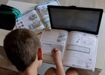 Niño haciendo deberes con tablet y libro, ejemplo de deberes digitales en colegios.