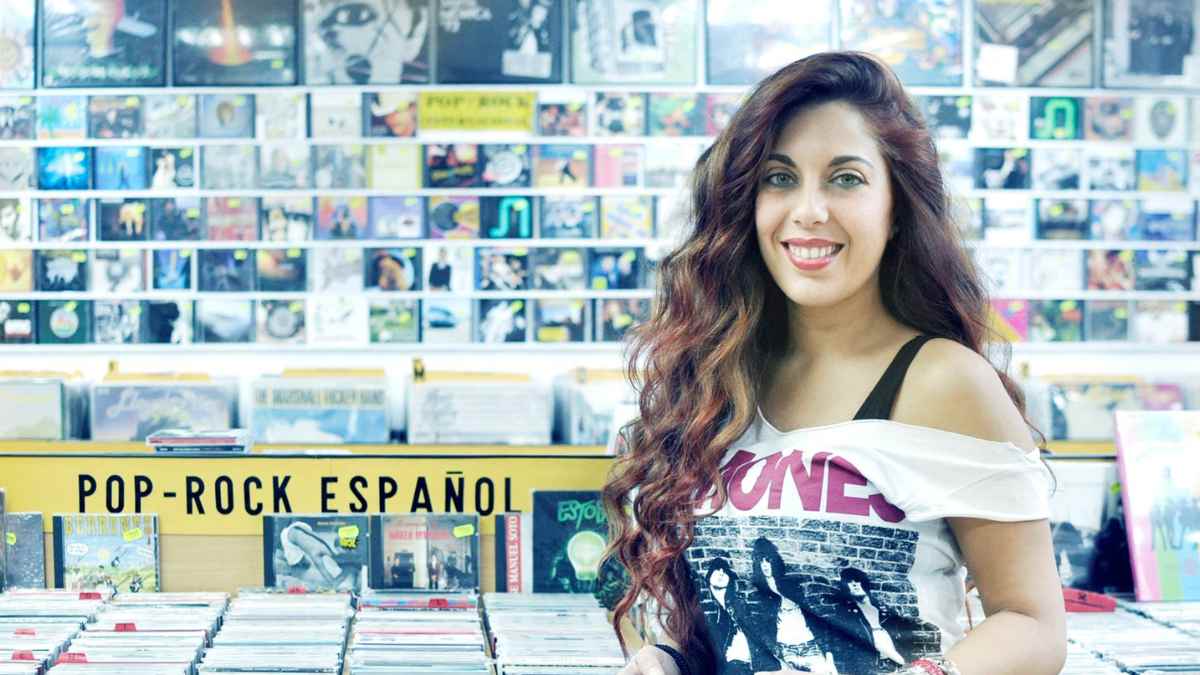 Interior de Discos La Metralleta en Madrid con mujer sonriendo junto a estanterías de vinilos y CD de pop-rock español.
