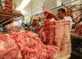 Carnicero trabajando en un mercado, con carne apilada para la venta.