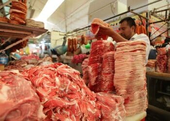 Carnicero trabajando en un mercado, con carne apilada para la venta.