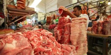 Carnicero trabajando en un mercado, con carne apilada para la venta.