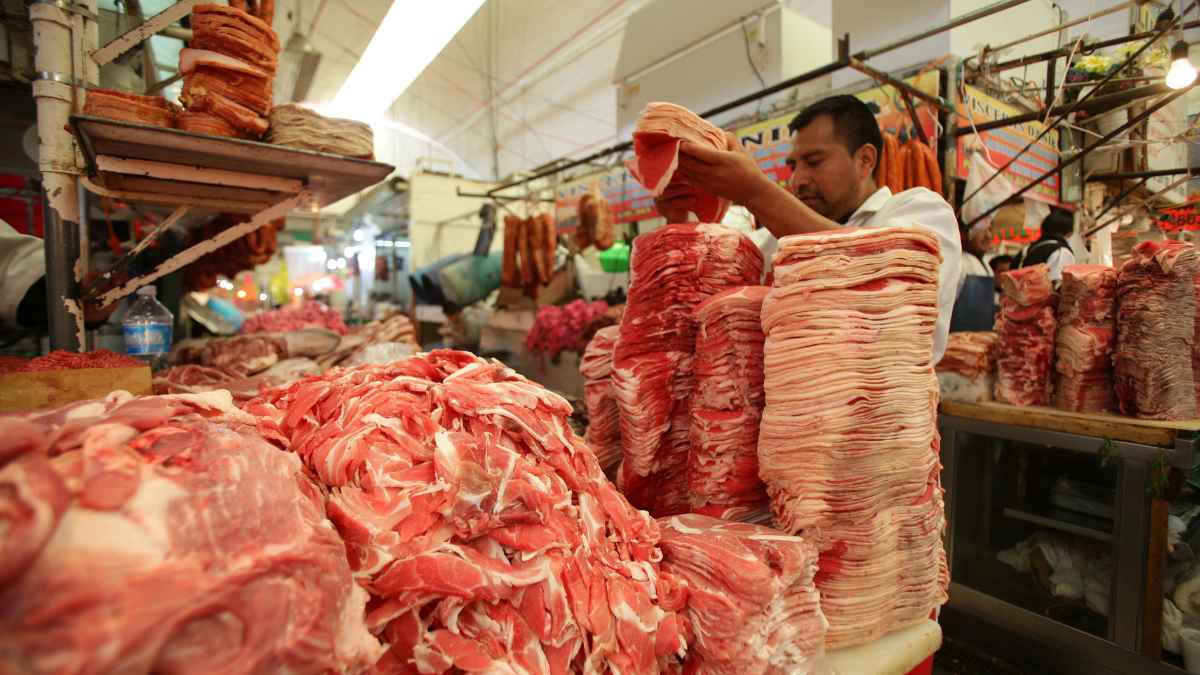 Carnicero trabajando en un mercado, con carne apilada para la venta.
