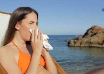 Mujer enferma en la playa estornudando durante sus vacaciones y con derecho a recuperar los días libres.