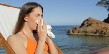 Mujer enferma en la playa estornudando durante sus vacaciones y con derecho a recuperar los días libres.