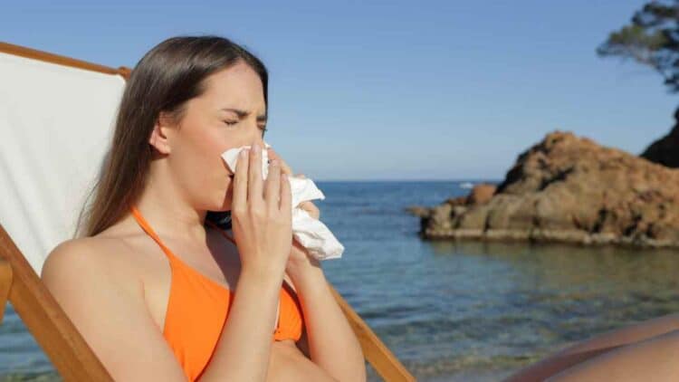Mujer enferma en la playa estornudando durante sus vacaciones y con derecho a recuperar los días libres.