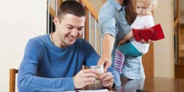 Padre contando dinero junto a madre con bebé, familias que obtienen hasta 1.462 € de ayuda económica del Ingreso Mínimo Vital.