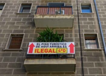 Cartel que indica que un piso turístico es ilegal en un edificio, con flechas y texto que señala la infracción.