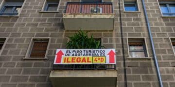 Cartel que indica que un piso turístico es ilegal en un edificio, con flechas y texto que señala la infracción.