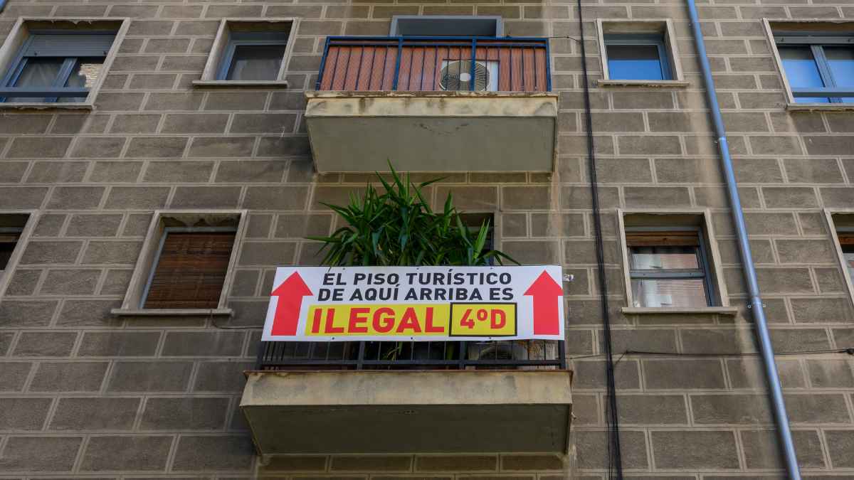 Cartel que indica que un piso turístico es ilegal en un edificio, con flechas y texto que señala la infracción.