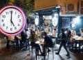 Terraza nocturna de un bar en Madrid llena de clientes, con un reloj marcando la medianoche que ilustra la ampliación de horario de cierre durante el Orgullo 2025.