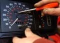Manos manipulando cuentakilómetros de coche con destornillador, posible delito de estafa.