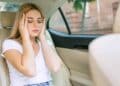 Mujer con dolor de cabeza en coche eléctrico, mareos y malestar.