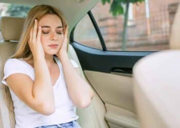 Mujer con dolor de cabeza en coche eléctrico, mareos y malestar.