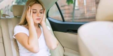 Mujer con dolor de cabeza en coche eléctrico, mareos y malestar.
