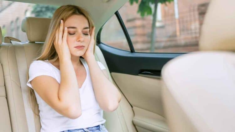 Mujer con dolor de cabeza en coche eléctrico, mareos y malestar.