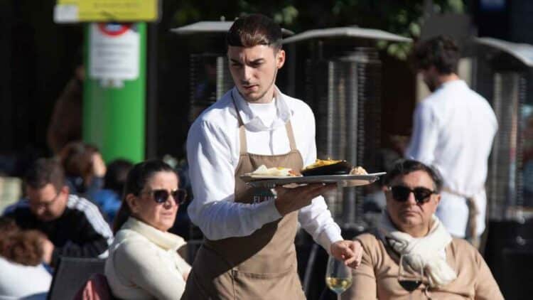 Camarero trabajando en una terraza, denuncia condiciones laborales oferta hostelería 1600 euros sin días libres.