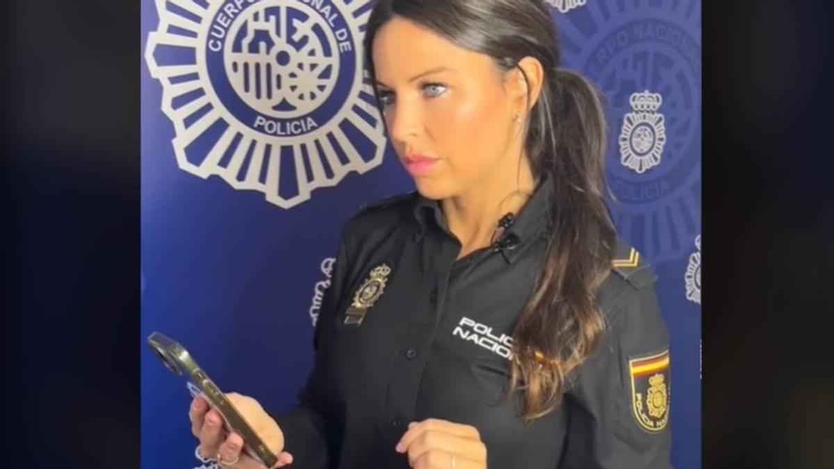 Agente de la Policía Nacional revisa un móvil mientras alerta sobre la estafa telefónica del prefijo exótico.