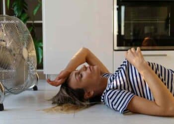 mujer acostada frente a ventilador doméstico, ejemplo de ahorro al dormir con ventilador cada noche en verano.