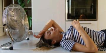 mujer acostada frente a ventilador doméstico, ejemplo de ahorro al dormir con ventilador cada noche en verano.