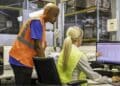 Trabajadores de almacén gestionan inventario en ordenador; sector logístico ofrece cinco ofertas de empleo con sueldos de hasta 30.000 euros.