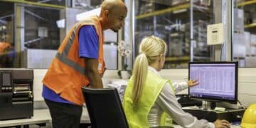 Trabajadores de almacén gestionan inventario en ordenador; sector logístico ofrece cinco ofertas de empleo con sueldos de hasta 30.000 euros.