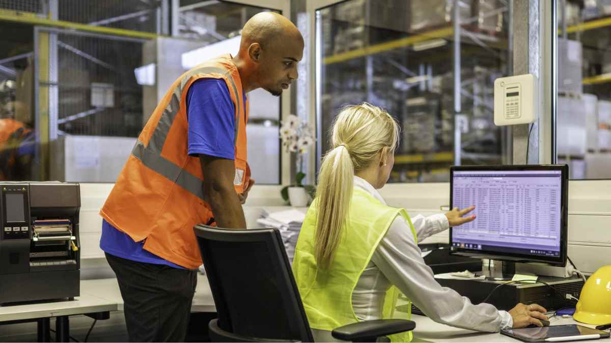 Trabajadores de almacén gestionan inventario en ordenador; sector logístico ofrece cinco ofertas de empleo con sueldos de hasta 30.000 euros.