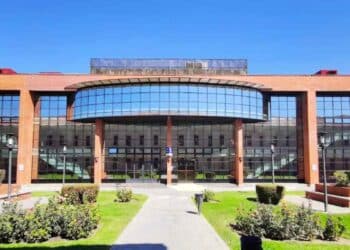 Fachada acristalada de una universidad pública madrileña con jardines, referente de los créditos más caros en España.