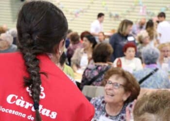 Voluntaria de Cáritas en Madrid conversa con personas mayores durante actividad solidaria de verano 2025.