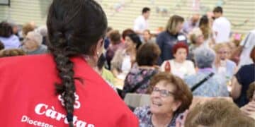 Voluntaria de Cáritas en Madrid conversa con personas mayores durante actividad solidaria de verano 2025.