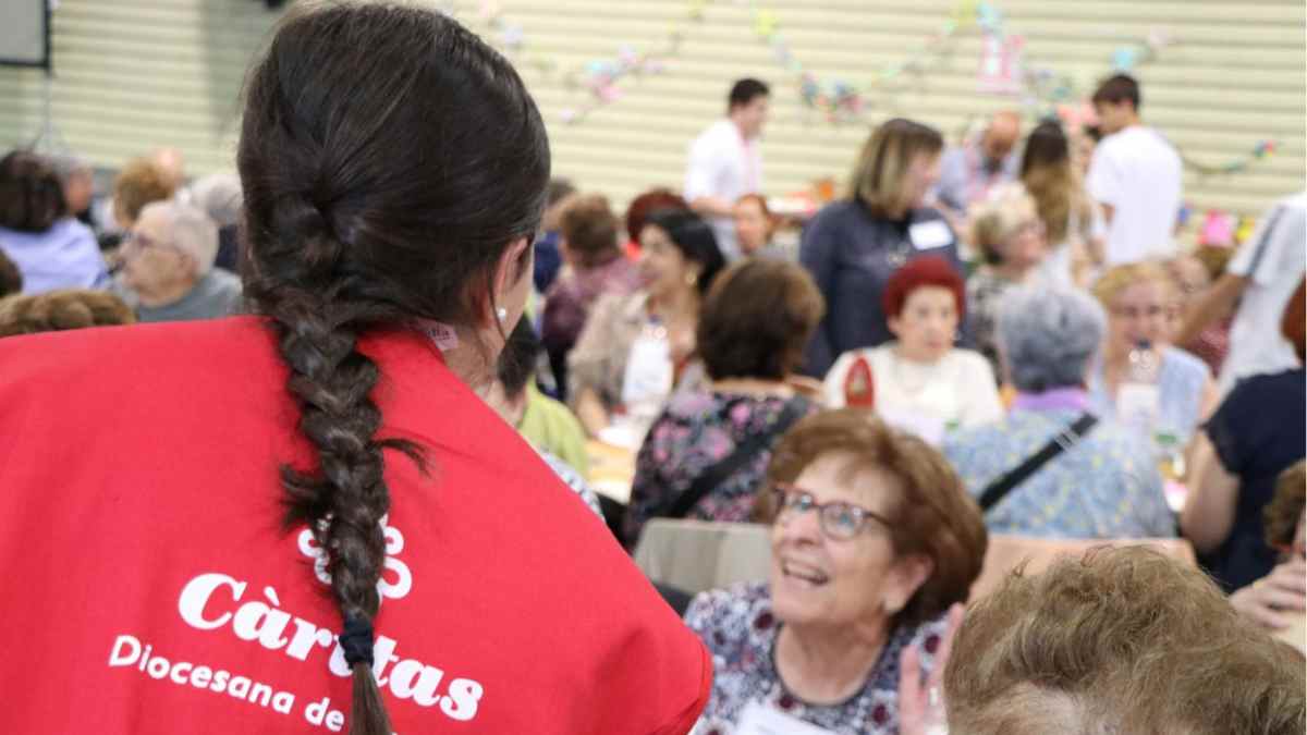 Voluntaria de Cáritas en Madrid conversa con personas mayores durante actividad solidaria de verano 2025.