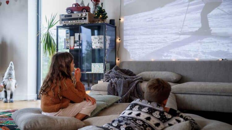 Familia viendo una película en casa usando un proyector, un ejemplo de cine en casa con proyector, pantalla y sofá.