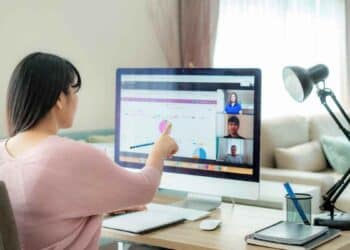 Mujer trabajando desde casa en videollamada y analizando gráficos en ordenador.