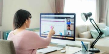 Mujer trabajando desde casa en videollamada y analizando gráficos en ordenador.