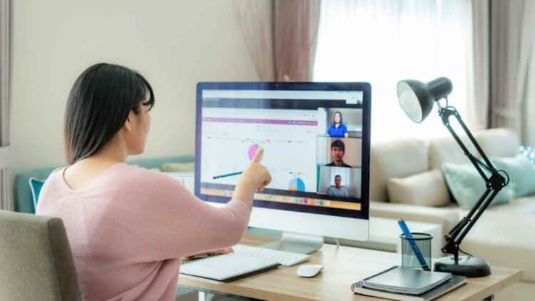 Mujer trabajando desde casa en videollamada y analizando gráficos en ordenador.