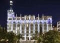 Fachada iluminada del Hotel ME Madrid Reina Victoria en la Plaza de Santa Ana durante la noche.