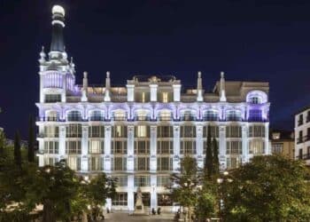 Fachada iluminada del Hotel ME Madrid Reina Victoria en la Plaza de Santa Ana durante la noche.