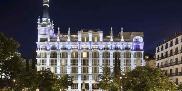 Fachada iluminada del Hotel ME Madrid Reina Victoria en la Plaza de Santa Ana durante la noche.