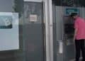 Hombre usando cajero automático con sucursal bancaria cerrada por festivo del 15 de agosto.