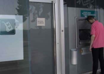 Hombre usando cajero automático con sucursal bancaria cerrada por festivo del 15 de agosto.
