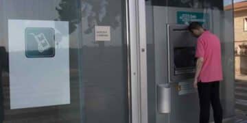 Hombre usando cajero automático con sucursal bancaria cerrada por festivo del 15 de agosto.